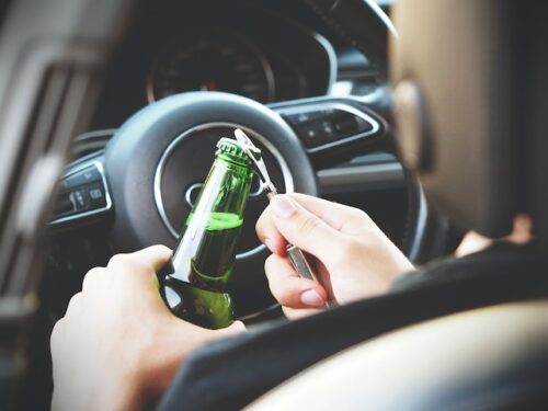 person opening a beer bottle behind the wheel